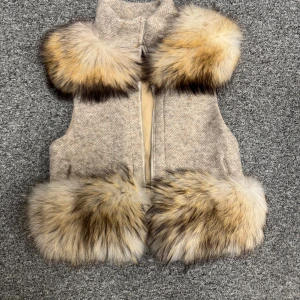 Beige pälsväst från Alessa - Snygg beige väst från Alessa med fluffiga pälsdetaljer i brunt, svart och vitt vid krage och nederkant. Västen har en rak passform, dragkedja framtill och är fodrad med ljusbeige tyg. Perfekt för att lyfta din outfit med en lyxig touch.