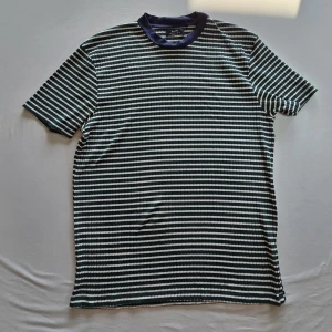 Randig t-shirt från Bershka - Säljer en randig t-shirt från Bershka i grönt, vitt och blått. T-shirten har korta ärmar och en blå ribbad krage. Perfekt för en avslappnad stil.