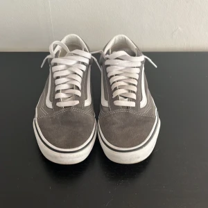 Gråa Vans - Säljer ett par klassiska Vans Old Skool sneakers i grå mocka med vita detaljer och vit sula. Skorna har snörning och den ikoniska sidoremsan i vitt. Perfekta för en avslappnad och stilren look. Har inga skador på sig.