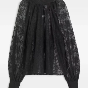 Svart spetsblus med rosett - Säljer en svart blus i transparent spets med stor rosett i nacken. Blusen har långa, vida ärmar med breda muddar och knappar vid ärmsluten. Perfekt för dig som gillar romantiska detaljer och elegant stil.