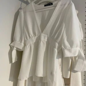 Vit blus med knytdetalj från Boohoo - Säljer en vit blus från Boohoo med v-ringning och trekvartsärmar som har knytdetalj vid ärmslut. Den sitter lite tajtare vid midjan. Helt oanvänd och i nyskick. 