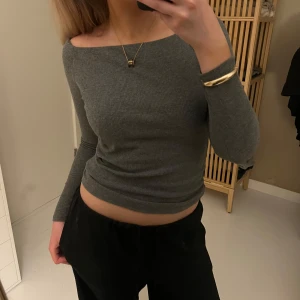Grå ribbad långärmad topp - Säljer en grå ribbad långärmad topp med båtringad hals. Toppen är tight och har en enkel, stilren design som passar perfekt till många olika outfits.☺️