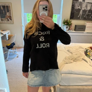 Zadig & Voltaire  - Säljer en svart stickad tröja med vit text 'Rock & Roll' på framsidan. Tröjan har lång ärm, ribbade muddar och en klassisk passform. Perfekt för dig som gillar en cool och avslappnad stil.