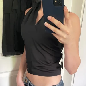 Svart knyttopp från Bik Bok - Säljer en svart knyttopp från Bik Bok i storlek XS. Toppen har knytning i nacken och smockad rygg för en bekväm passform. Perfekt till sommaren och enkel att styla med jeans eller kjol. Använd en gång.