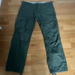 Gröna cargobyxor från Carhartt WIP - Säljer ett par gröna cargobyxor från Carhartt WIP i storlek 36/32. Byxorna har flera praktiska fickor på sidorna och bak, samt klassisk Carhartt-logga på ena benet. Perfekta för dig som gillar funktionella och stilrena byxor.