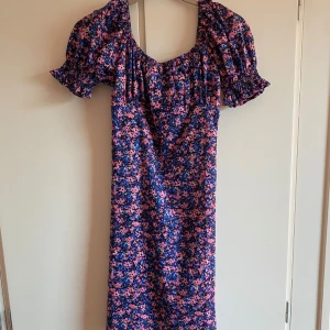 Blommig långklänning med puffärmar - Säljer en långklänning med blå och rosa blommigt mönster. Klänningen har puffiga kortärmar och smockad rygg för extra komfort. Perfekt för dig som gillar färg och vill sticka ut med en romantisk stil.