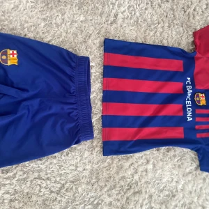 FC Barcelona fotbollströja och shorts - Säljer en klassisk FC Barcelona fotbollströja med blå och röda ränder samt tillhörande blå shorts. Tröjan har klubbens logga och texten FC BARCELONA på bröstet. Perfekt för dig som älskar Barca!
