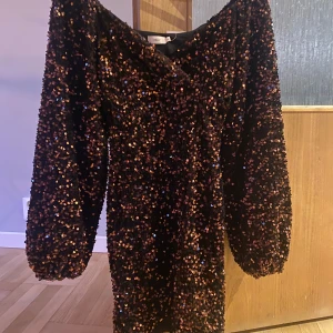 Svart paljettklänning med puffärmar från Nelly - Säljer en kort klänning från Nelly täckt av glittriga paljetter i koppar och är figursydd. Helt ny och lapp finns kvar.