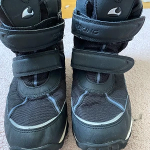 Svarta vinterkängor från Viking - Svarta vinterkängor från Viking med två breda kardborreband för enkel påtagning. Grov sula för bra grepp och förstärkta partier runt tån och hälen. Skorna har diskreta grå detaljer och är tillverkade i syntetmaterial. 