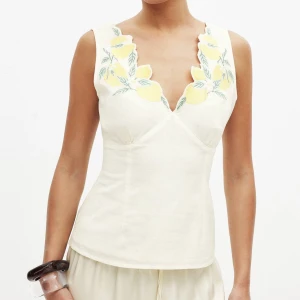 Vit linnetopp med citronbroderi - Superfin vit linnetopp med broderade gula citroner och gröna blad längs den v-ringade halsen. Toppen är ärmlös och har en snygg v-ringning både fram och bak. Perfekt för sommardagar och ger en fräsch känsla.