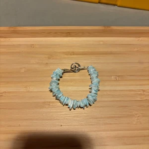 Blått armband med oregelbundna stenar - Säljer ett snyggt armband med ljusblå oregelbundna stenar och ett dekorativt silverfärgat lås. Perfekt för dig som vill ha något unikt och stilrent till din accessoarsamling.