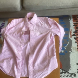 Ljusrosa skjorta från Polo Ralph Lauren - Säljer en klassisk ljusrosa skjorta från Polo Ralph Lauren i storlek M. Skjortan har lång ärm, knappar framtill och button-down krage. Perfekt för dig som gillar stilrena och tidlösa plagg med en preppy känsla. Köpt på nk  den passar om man är runt 145cm lång
