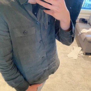 Mörkgrön linne overshirt från Massimo Dutti - Säljer en stilren mörkgrön skjorta från Massimo Dutti i 100% linne. Skjortan har klassisk krage, knäppning framtill och två bröstfickor med lock. Perfekt för dig som gillar en avslappnad men snygg look.