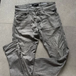 Gråa slim fit jeans från Replay  - Säljer ett par gråa Replay Anbass jeans i slim fit-modell. Klassisk femficksdesign, snygga detaljer och bekväm passform. Perfekta för dig som gillar stilrena och moderna jeans. Midjemått W31 och längd L32.