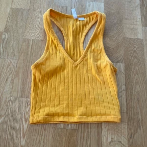 Gul ribbad croppad linnetopp - Säljer en solgul croppad linnetopp med ribbad struktur och djup v-ringning. Toppen har brottarrygg och är ärmlös, perfekt för varma dagar eller lager på lager.