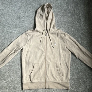 Beige hoodie från Polo Ralph Lauren - Säljer en beige hoodie från Polo Ralph Lauren i storlek M. Tröjan har dragkedja, huva med snörning och två fickor där fram. I princip ny skick då den har använt ungefär 5 gånger, därför riktigt fräsch utan defekter. Hör av dig om du har frågor! Köparen står för frakt.