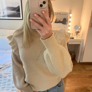 Beige stickad tröja med volang från VILA - Säljer en beige stickad tröja från VILA med fina volangdetaljer på axlarna. Mycket mjukt material och en hög hals. Använd fåtal gånger, i mycket bra skick. Storlek L men passar flera storlekar som S/M☺️