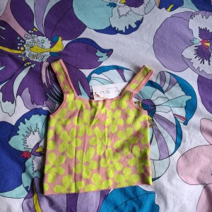 Blommig croppad linnetopp från Aisui - Superfin croppad topp från Aisui i rosa med stora limegröna blommor. Tjockare axelband och fyrkantig halsringning. Perfekt för sommardagar när du vill sticka ut lite extra!