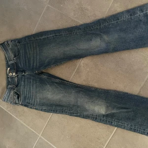 Blå bootcut jeans från Gina Tricot - Säljer ett par klassiska blå jeans från Gina Tricot i modell bootcut. Jeansen har låg midja, fem fickor och stängs med dragkedja och knapp. Snyggt slitna detaljer framtill och bakfickor med sömmar. Säljer pga är för små på mig