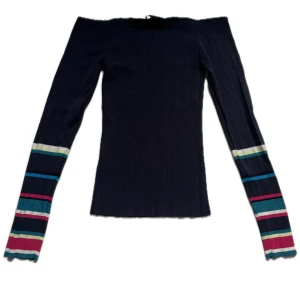 Svart ribbad offshoulder-tröja med färgglada ränder - Säljer en svart ribbad offshoulder-tröja från Sandro med långa ärmar. Ärmarna har färgglada ränder i blått, grönt, rött, rosa och gult. Perfekt för dig som vill sticka ut med en cool och trendig look.