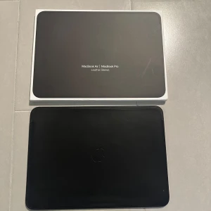 Svart läderfodral till MacBook Air/Pro från Apple - Säljer ett stilrent svart läderfodral från Apple som passar MacBook Air och MacBook Pro 13-tum. Fodralet har en minimalistisk design med Apple-logga och är perfekt för att skydda din laptop när du är på språng. Aldrig använd, helt ny. 