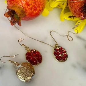 Granatäpple örhängen och halsband i guld och rött - Unika örhängen och halsband formade som granatäpplen med guldfärgad ram och röda detaljer som liknar kärnor. Perfekta för dig som vill sticka ut med ett färgglatt och fruktinspirerat smycke.