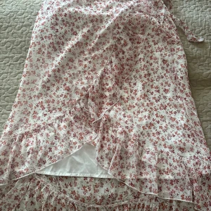 Blommig kjol från Vero Moda - Supersöt vit kjol från Vero Moda med små rosa och röda blommor. Kjolen har volangdetaljer längs nederkanten och bnytbar rosett i midjan. Perfekt för sommarens alla tillfällen! Skicka om ni har frågor eller vill ha fler bilder🫶🏻 storlek L💞 det är stretch i midjan💞ej använd alls🩷