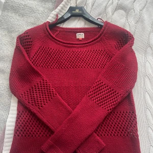 Vinröd stickad tröja från ONLY - Säljer en vinröd stickad tröja från ONLY med lång ärm. Tröjan har ett snyggt hålmönster i breda ränder och rund halsringning. Perfekt för lager-på-lager och höst- eller vinteroutfits.