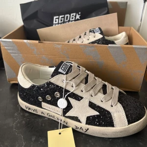 Golden Goose golden day - Säljer ett par Golden Goose sneakers i svart med glittrig ovandel och den klassiska stjärnan på sidan. Skorna har snörning, rund tå och texten 'Have a Golden Day' på sulan. Perfekta för dig som gillar unika detaljer och vill ha ett par sommarskor.