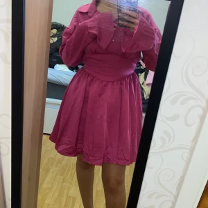 Rosa kortklänning med krage och vida ärmar - Säljer en rosa kortklänning med markerad midja, krage och långa vida ärmar. Klänningen har en lätt utställd kjol och knappar framtill vid halsen. Perfekt för dig som vill sticka ut med en färgstark look!