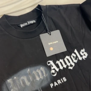 Svart t-shirt från Palm Angels med tryck - Helt oanvänd och priset hår att diskutera Säljer en svart t-shirt från Palm Angels med ikoniskt vitt tryck framtill där det står 'Palm Angels Paris'. T-shirten har rund hals och korta ärmar. Materialet är 100% polyester och modellen är normal passform.