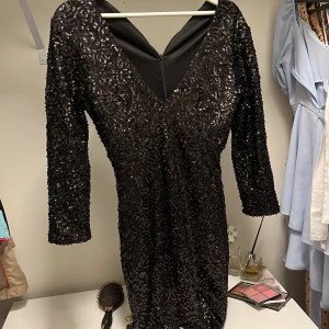Svart paljettklänning från NLY One - Säljer en svart glittrig klänning från NLY One med paljetter över hela ytan. Klänningen har v-ringning, trekvartsärm och en figurnära passform. Perfekt för dig som vill sticka ut på festen!
