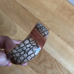 Handmade Bred armband med ormskinnsmönster - Säljer ett brett armband i brun och beige med svart ormskinnsmönster. Armbandet har en glansig yta och är ett statement-smycke som verkligen sticker ut på handleden.