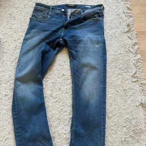Blå Replay jeansbyxor - Säljer ett par klassiska blå jeans från Replay med fem fickor och snygga slitningar. Byxorna har normal passform och raka ben. Märkeslapp bak i midjan och dragkedja i gylfen. Perfekta till vardags för en avslappnad stil. Dm för frågor!