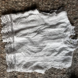 Vit spetsblus från Sim & Sam - Säljer en superfin vit blus från Sim & Sam med vackra spetsdetaljer och broderade mönster. Blusen är ärmlös och har dekorativa kanter nertill och vid ärmhålen. Perfekt för vår och sommar! Strl M men passar mig som är strl XS-S.