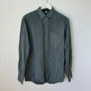 Grå Arket skjorta i lyocell - Säljer en stilren grå skjorta i 100% lyocell med klassisk krage och bröstficka. Skjortan har långa ärmar och knäppning framtill. Perfekt för dig som gillar en enkel och clean look. Artnr: Ö301