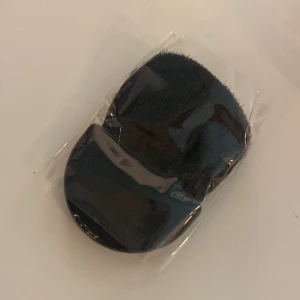 Svart kompakt sminkborste - En kompakt och platt sminkborste med svart borst och svart handtag. Perfekt för applicering av bronzer eller rouge. Borsten är mjuk och lätt att använda för att blenda ut smink jämnt över huden. Helt ny aldrig använt 