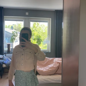 Beige croppad jeansjacka med knappar - Säljer en beige croppad jeansjacka från Zara med silverfärgade knappar och två bröstfickor. Jackan har klassisk krage och långa ärmar. Perfekt att slänga över en t-shirt eller klänning för en chill look.