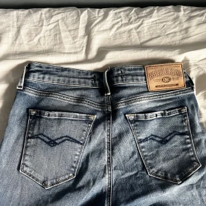 Blå jeansbyxor från Replay - Snygga blå jeans från Replay med klassisk femficksdesign och läderpatch bak i midjan. Jeansen har raka ben och subtila slitningar framtill. Perfekta för en avslappnad och stilren look.