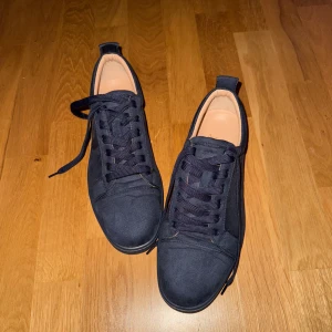 Mörkblå sneakers från Christian Louboutin - Säljer ett par mörkblå sneakers från Christian Louboutin med klassisk röd sula och snörning. Skorna har rund tå och är tillverkade i mocka med diskret logga på innersulan. Perfekta för dig som gillar stilrena och exklusiva sneakers. Använda en gång.