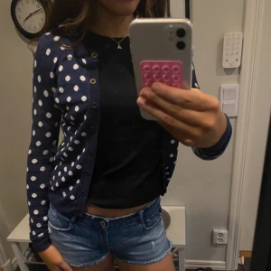 Mörkblå prickig kofta - Säljer en söt mörkblå kofta med vita prickar och svarta knappar. Koftan har lång ärm och rund halsringning. Perfekt att slänga över en topp eller linne, så fint nu till sommaren💘