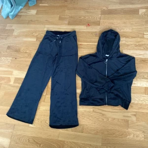 Svart mjukis sett från 157 - Svart mjukis sett från 157 med resår och snörning i midjan. Byxorna har raka ben och är tillverkade i ett mjukt och bekvämt material som passar perfekt för en avslappnad stil. Koftan är också skön och mysig och d passar parfekt till vintern/hösten