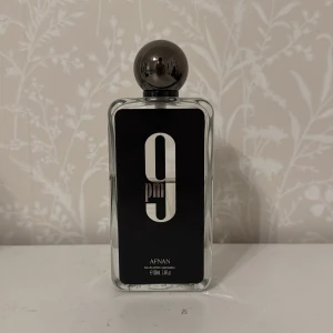 Afnan 9pm Eau de Parfum 55-60ml - Afnan 9pm är en herrparfym i en stilren, rektangulär glasflaska med svart etikett och stor silverfärgad rund kork. Flaskan rymmer 100 ml och har en modern, minimalistisk design med siffran 9 i vitt på framsidan.