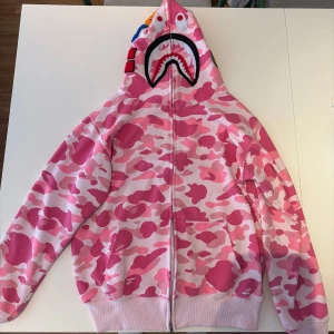 BAPE Rosa camo hoodie  - Säljer en rosa camo hoodie från BAPE med dragkedja och ikonisk hajdesign på huvan. 