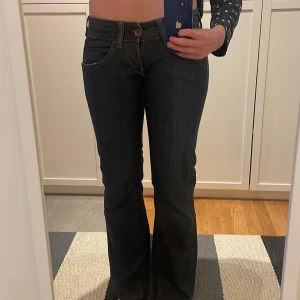 Mörkblå bootcut jeans Replay - Säljer ett par mörkblå jeans med bootcut passform och låg midja. Jeansen har klassiska fickor fram och bak, samt snygga kontrastsömmar. Perfekta för dig som gillar en retroinspirerad stil. ‼️Jag på bilden har midjemått 82 och är typ 175, de går ner till fötterna‼️