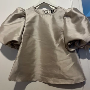 Beige blus med puffärmar - Superfin beige glansig topp med puffärmar. 🤎Använd 1 gång då den är lite för stor för mig! Priset kan diskuteras
