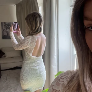 Vit spetsklänning med lång ärm - Superfin vit spetsklänning med långärmade ärmar och v-ringning i ryggen. Klänningen är figurnära och har vackra spetsdetaljer över hela tyget. Perfekt för student eller sommarens fester!