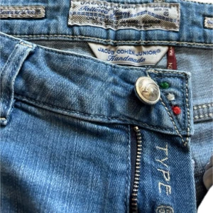 Blå jeans från Jacob Cohën Junior Type 696 - Säljer ett par klassiska blå jeans från Jacob Cohën Junior, modell Type 696. Jeansen har normal passform, dragkedja och knapp framtill samt diskreta detaljer i rött, grönt och vitt vid linningen. Mått längd 102cm brädd 37cm