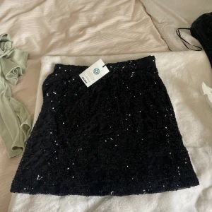 Svart glittrig kjol - Säljer en svart kjol med massor av paljetter som ger ett riktigt glittrigt intryck. Kjolen har en rak passform och är perfekt för dig som vill sticka ut. Supersnygg att styla med en enkel topp eller kavaj.