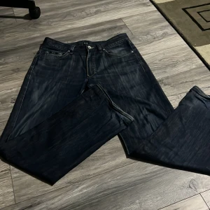 Mörkblå hugoboss jeans - Säljer ett par klassiska mörkblå hugoboss jeans med raka ben och fem fickor. Byxorna har knapp- och dragkedjegylf samt diskreta slitningar framtill för en snygg vardagslook.